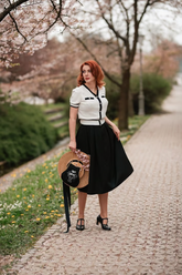 a lady in a white cardigan with black trim and a black skirt
